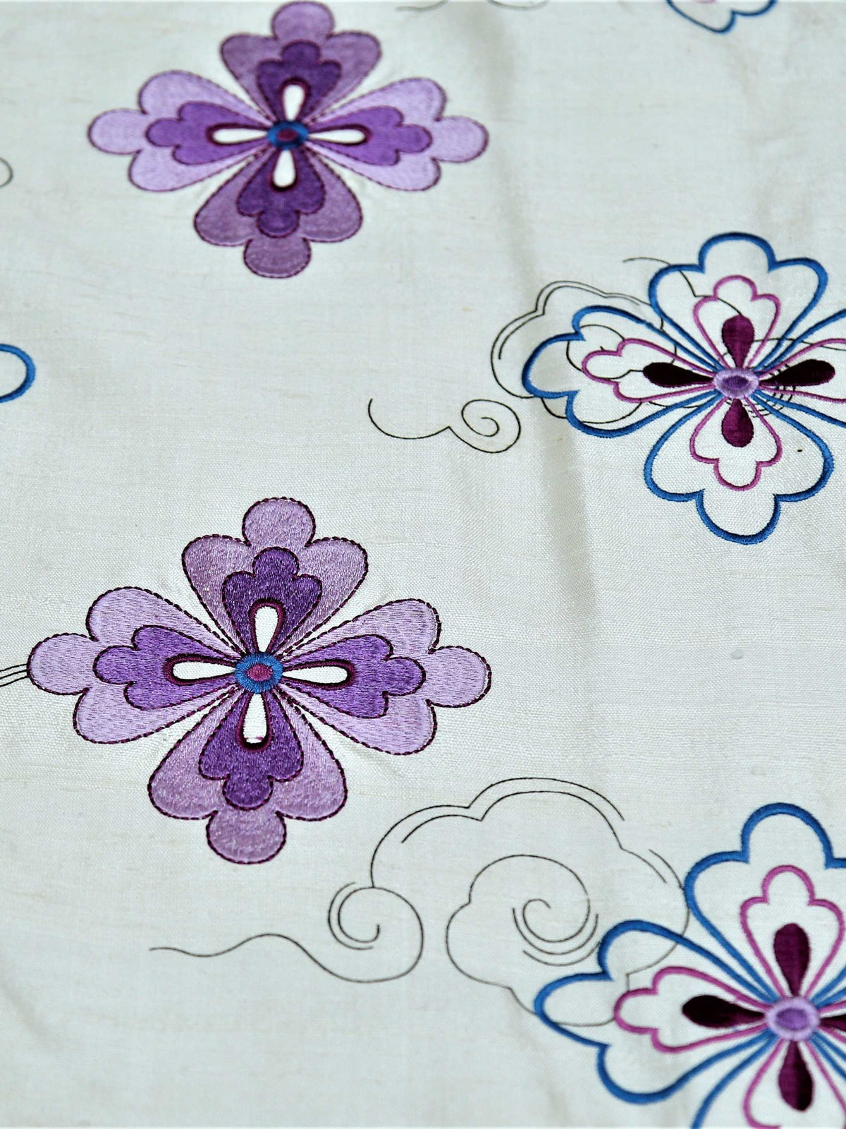 Close up of white polysilk embroidered with purple and blue flowers and fine scrollwork