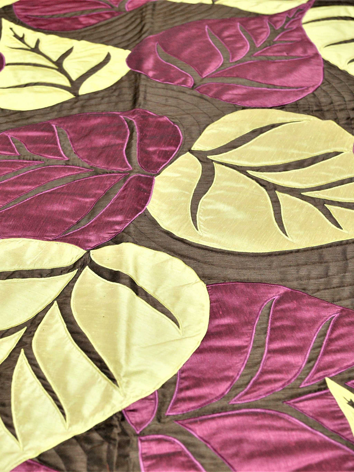 Close-up of cream and aubergine silk leaf applique on quilted brown ground
