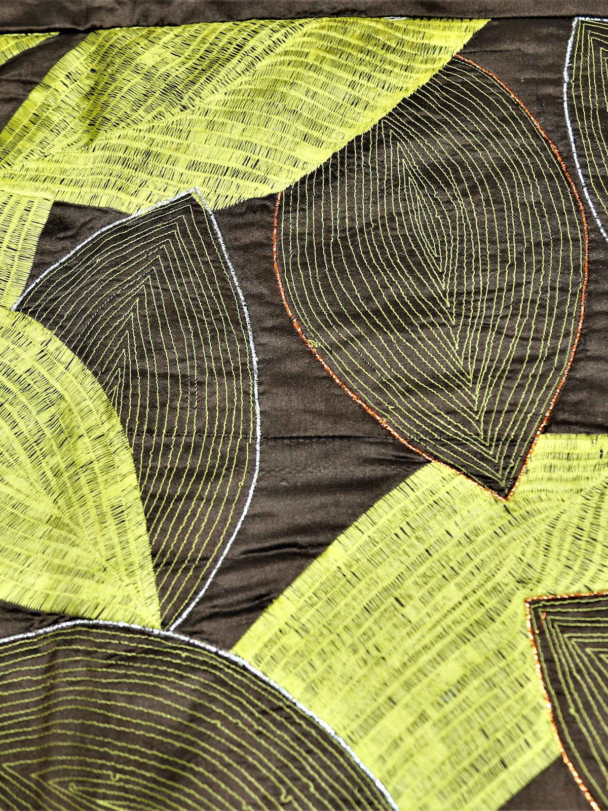 Close up of dark brown fabric embroidered with overlapping lime green leaves