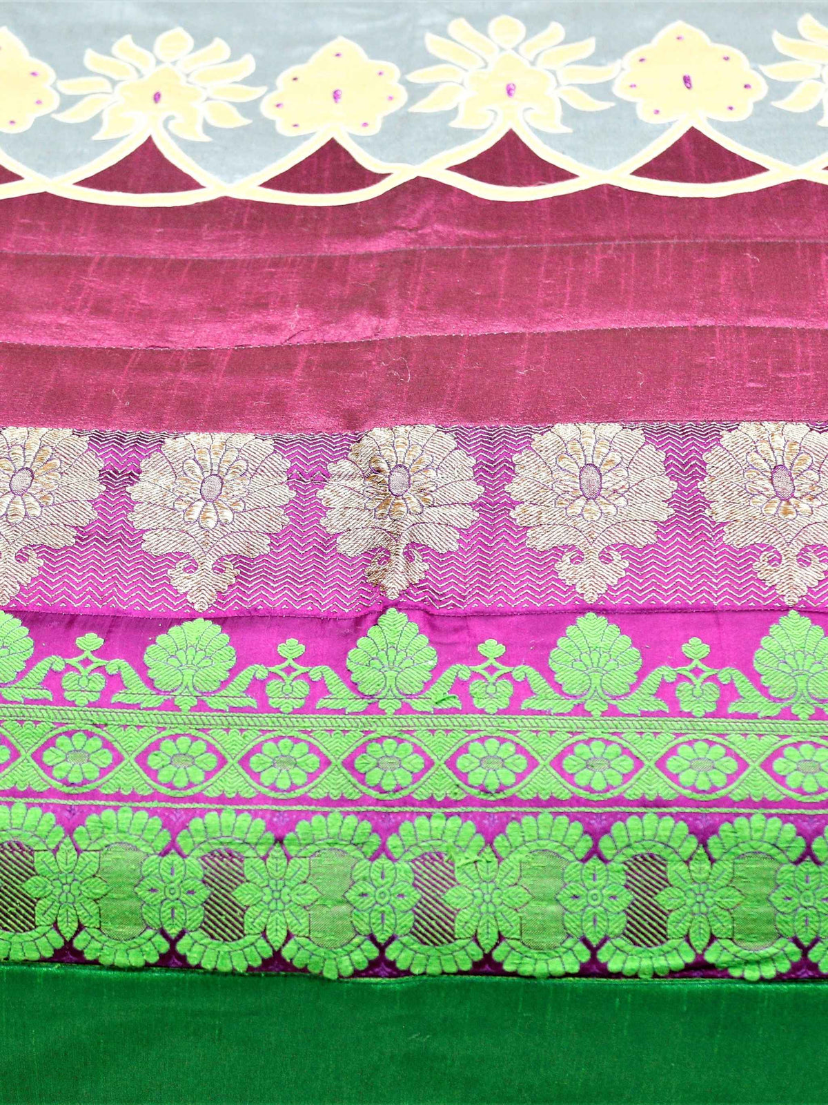 Close-up of green and gold zari brocade bands with cream floral cutwork on magenta silk