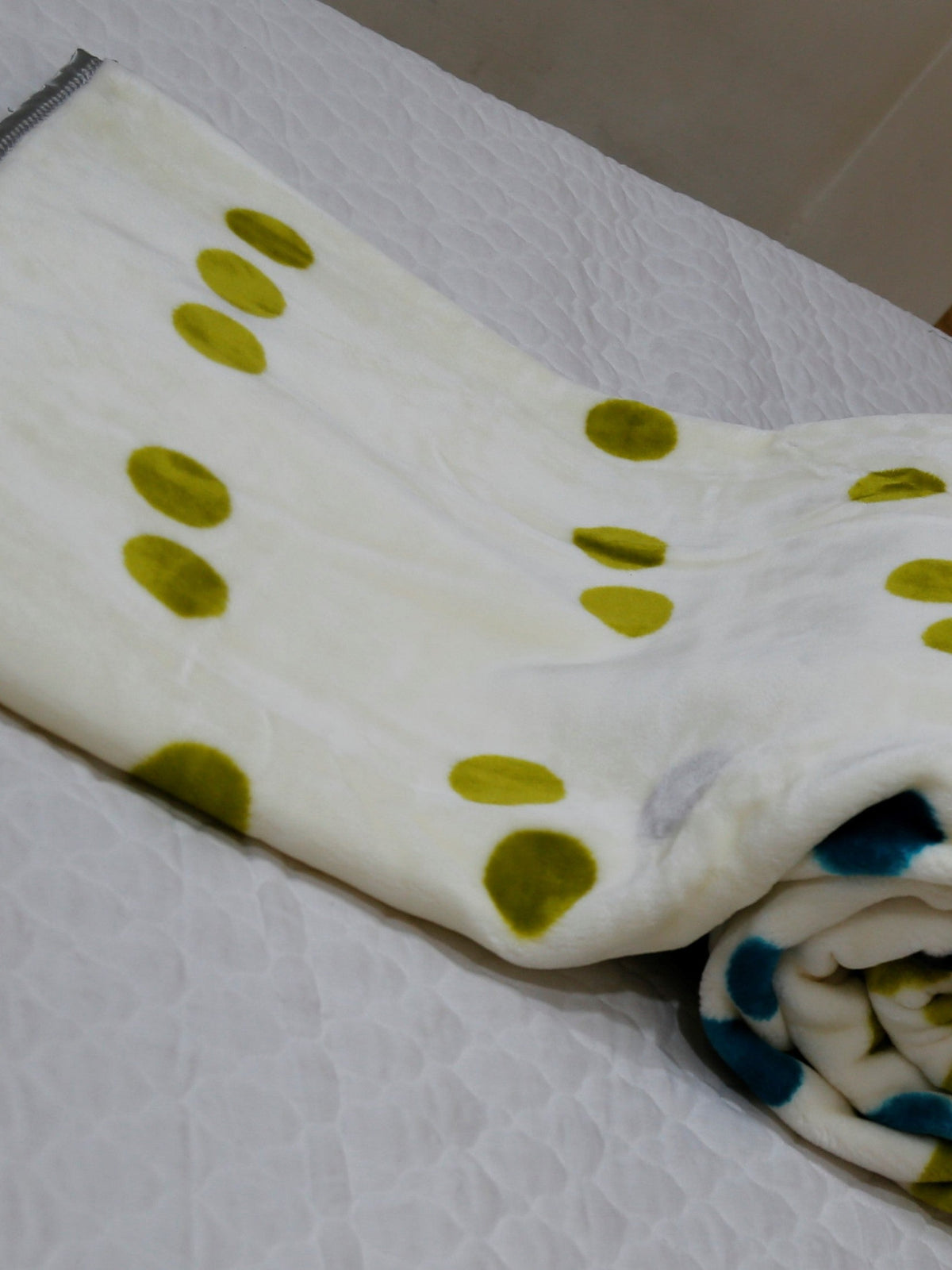 White-cream blanket folded to show mostly olive-green polka dots, with a rolled navy-teal edge