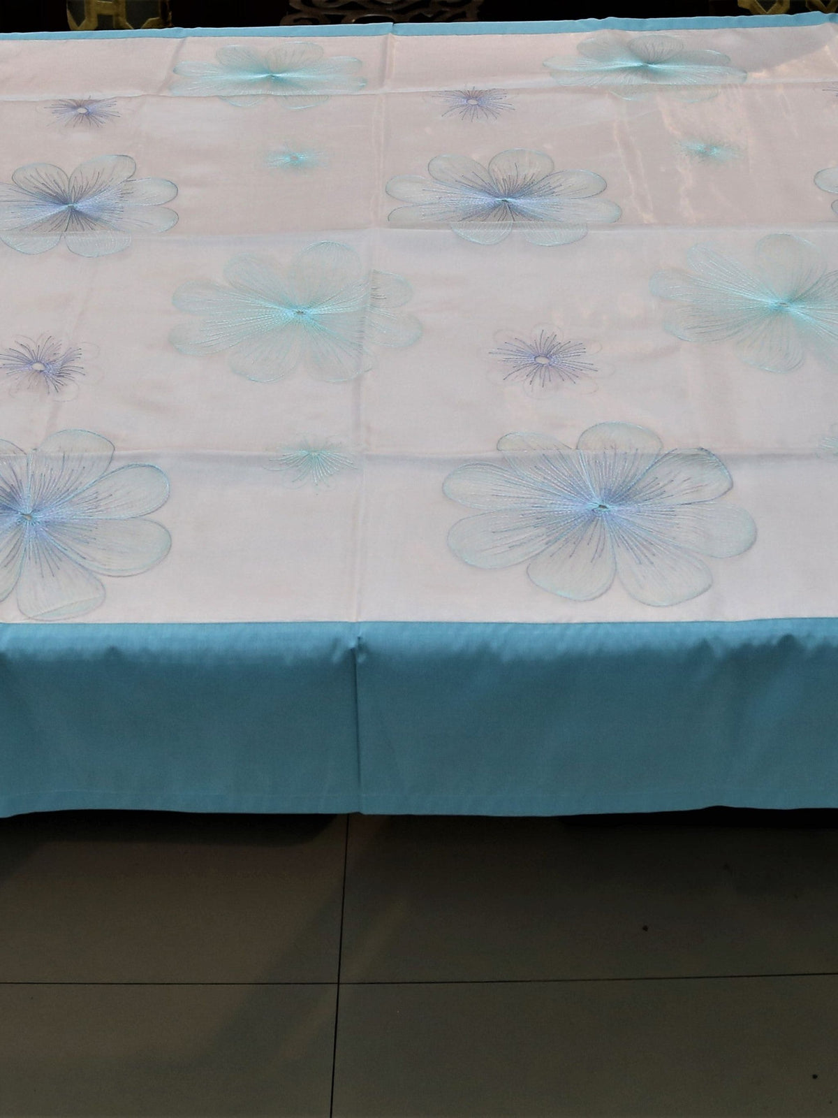 White oval table cover with a blue and purple embroidered flower pattern and a solid teal-blue border