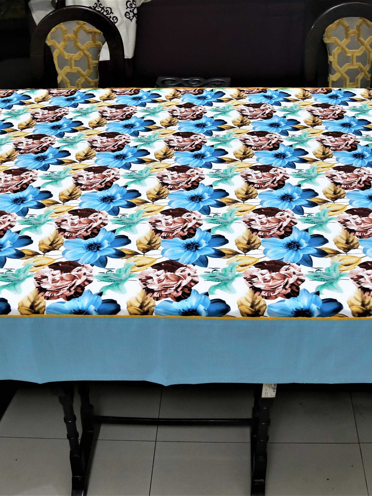 White table cover with a large blue, brown, and teal floral print and a solid light-blue underskirt with gold piping