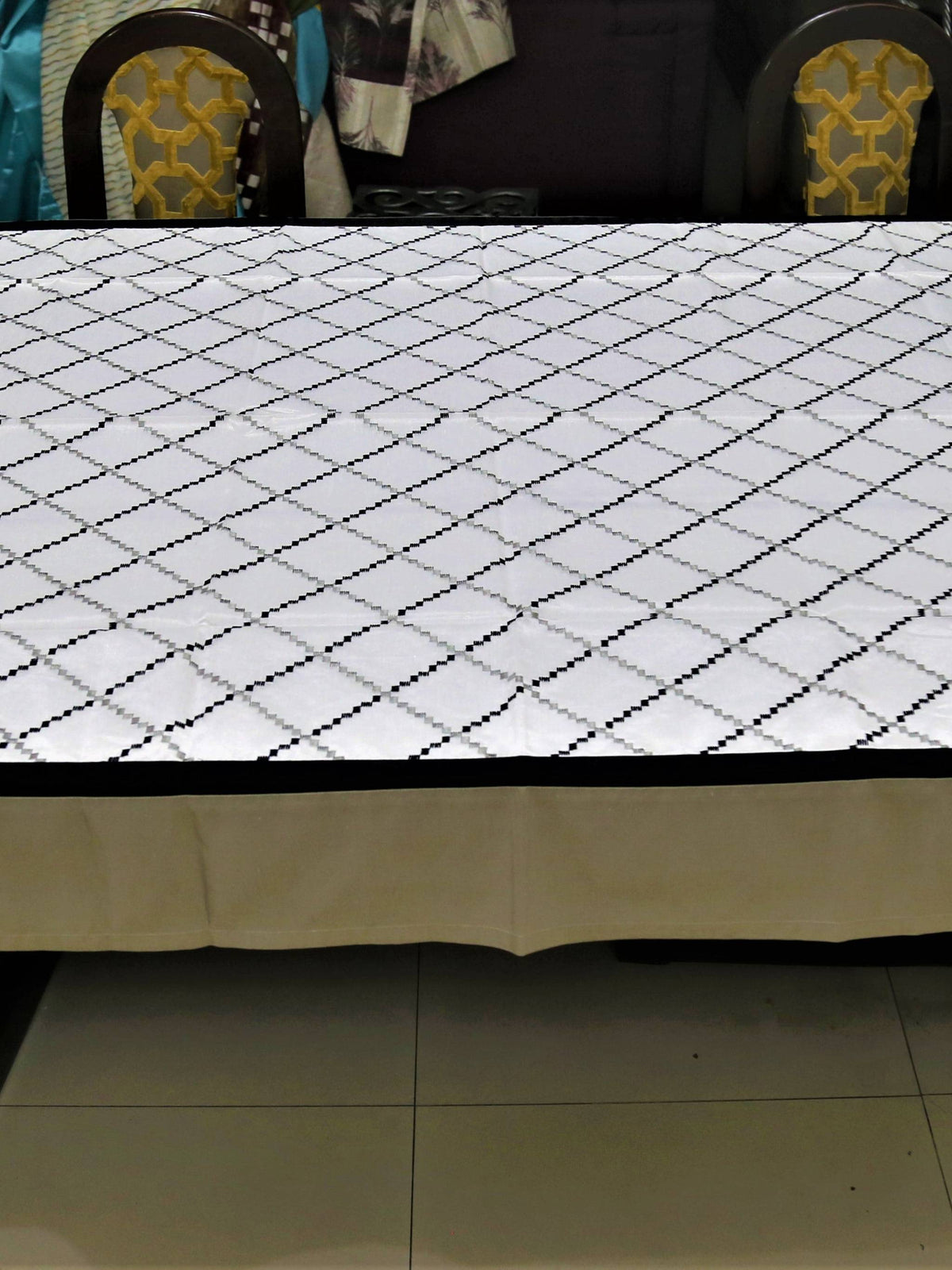White table cover with a black and grey diamond-lattice embroidered pattern and a plain beige-tan underskirt with a black edge trim