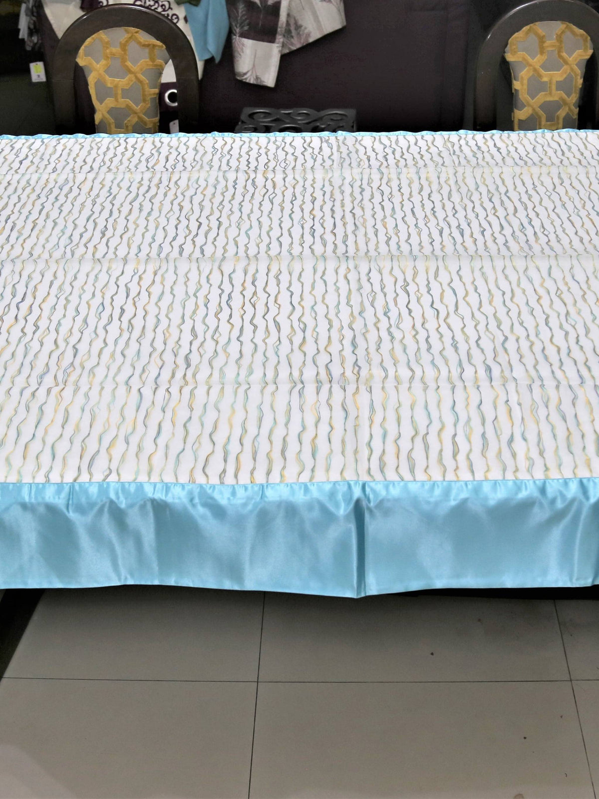 Cream table cover with a wavy multicolour stitch-line pattern and a solid sky-blue satin border