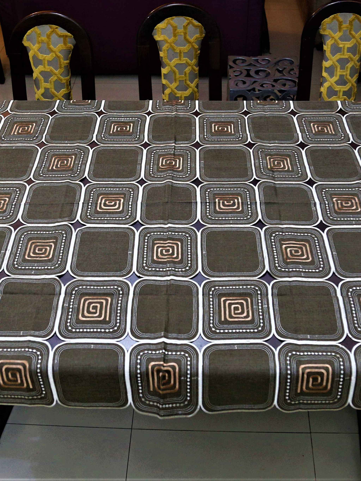 Brown table cover with a cutwork square pattern and copper spiral motifs inside each square
