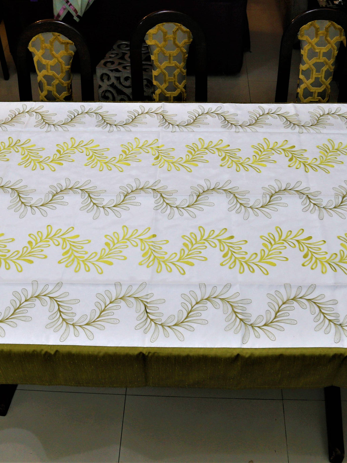 White table cover with a green and yellow embroidered fern-leaf vine pattern and a solid olive-green underskirt