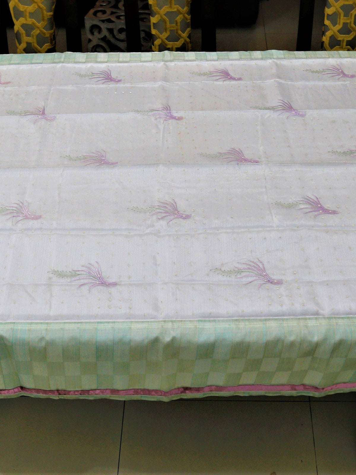 White table cover with lavender embroidered wheat-sprig motifs and scattered gold dots, with a mint-green checkered underskirt trimmed in pink
