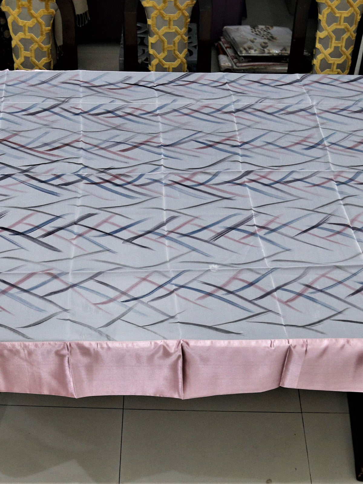 White table cover with a criss-crossing blue, pink, and grey stitch-line pattern and a solid blush-pink satin border