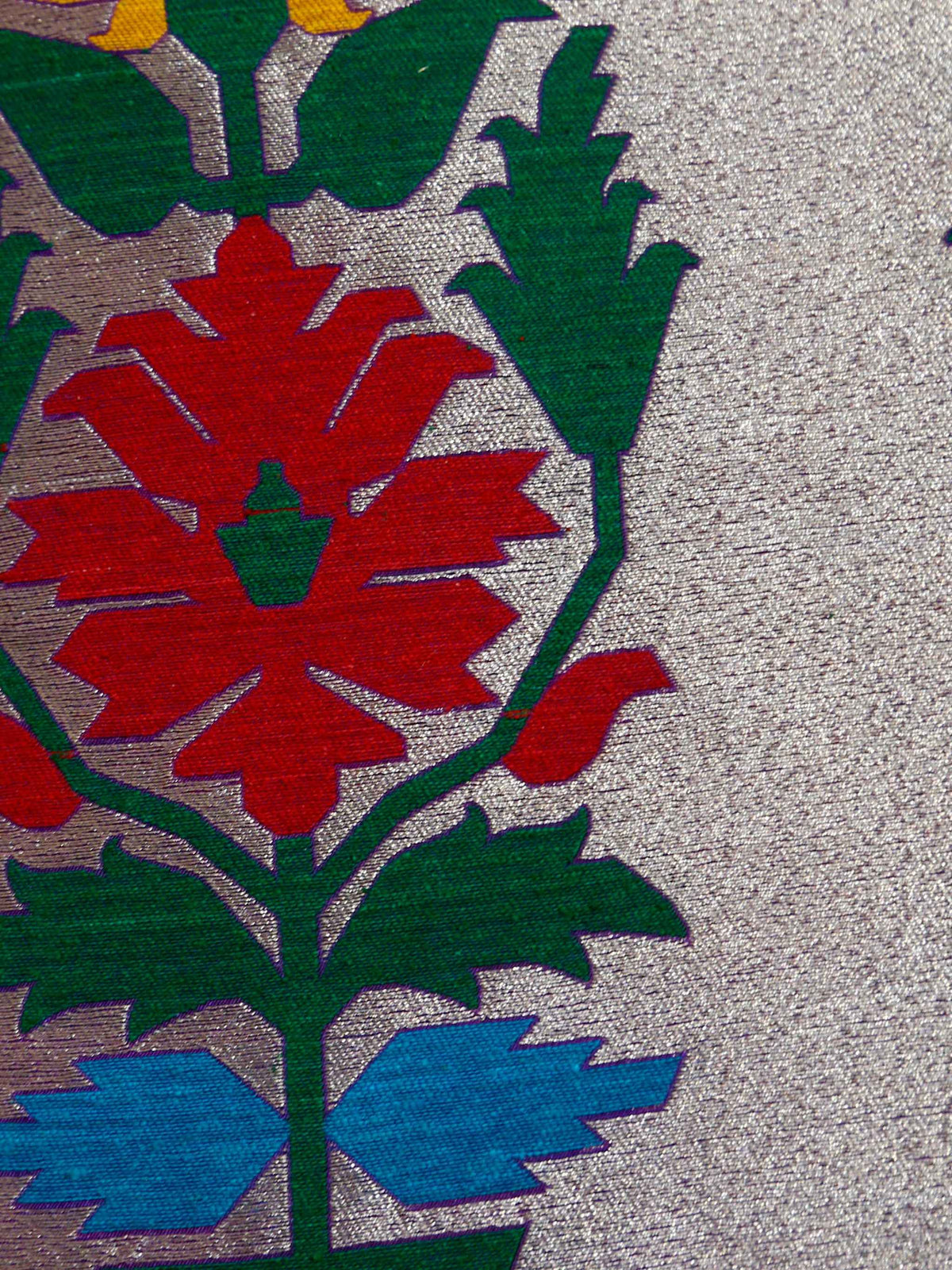 Close-up of the flowering vine woven in orange, red, green and blue on silver brocade