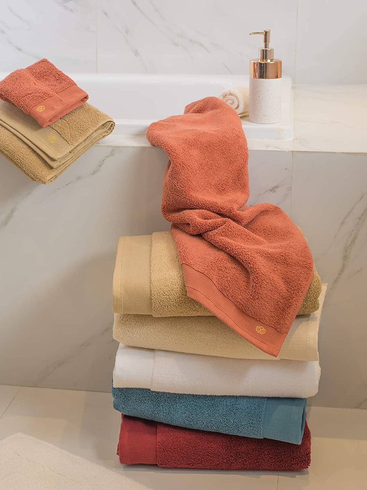 Stack of Micro Cotton bath towels in terracotta, beige, white, teal, and maroon on a bathroom shelf