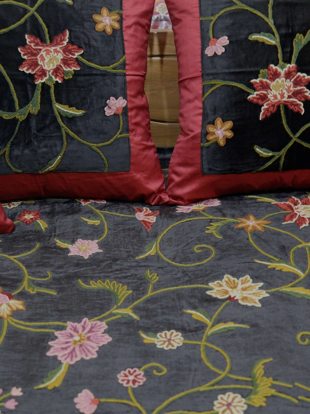 Close-up of the maroon and black velvet cushion covers against the floral-embroidered black bedcover