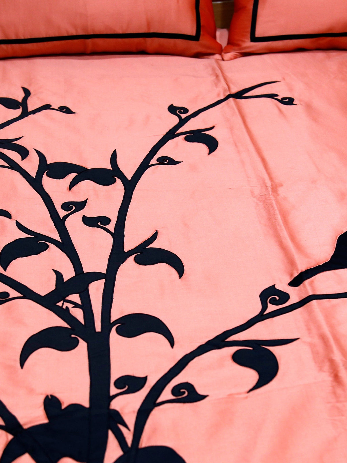 Close-up of black velvet bird and leafy branch applique on coral silk