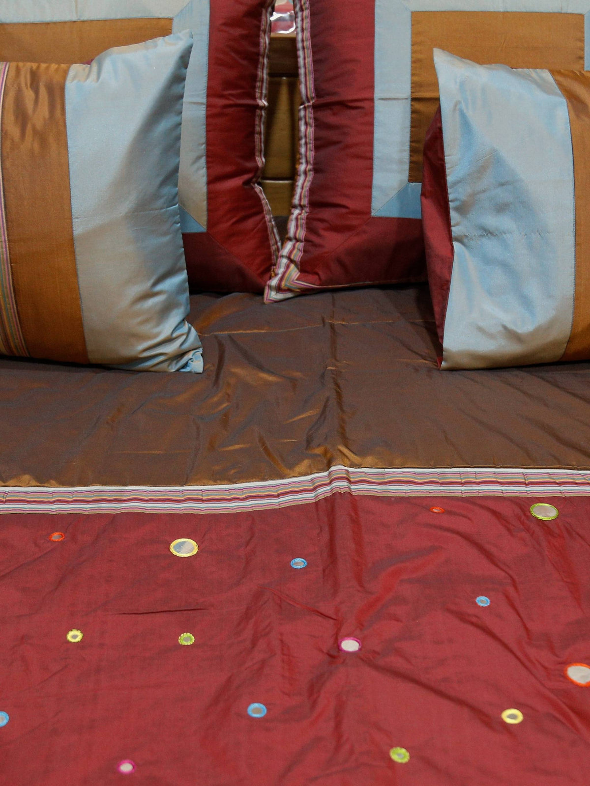 Close-up of coloured mirror work dots on maroon silk with striped cushion covers