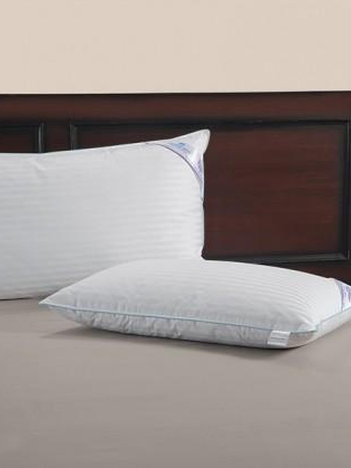 Two Regent satin stripe pillows on a made bed against a dark wooden headboard