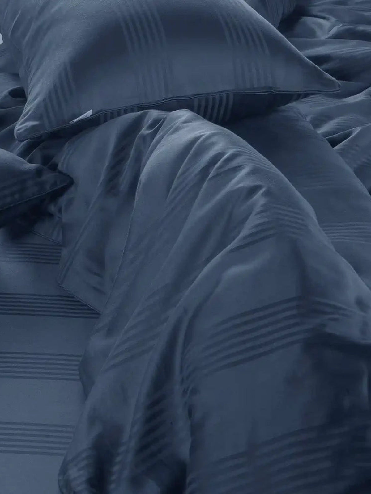 Denim blue satin stripe cotton sheet draped over a bed showing the woven stripe