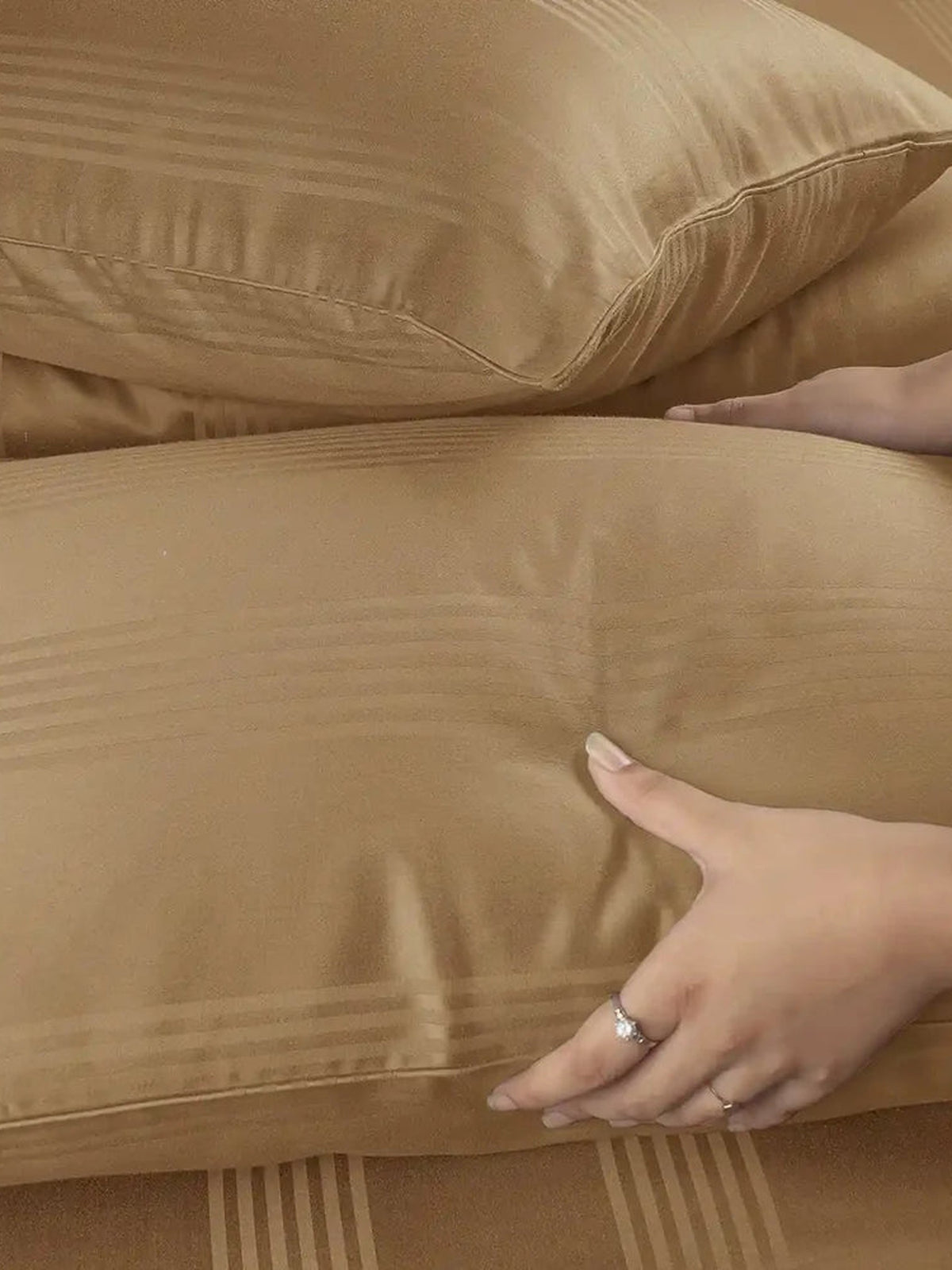Hands pressing camel tan satin stripe pillows to show the cotton's softness