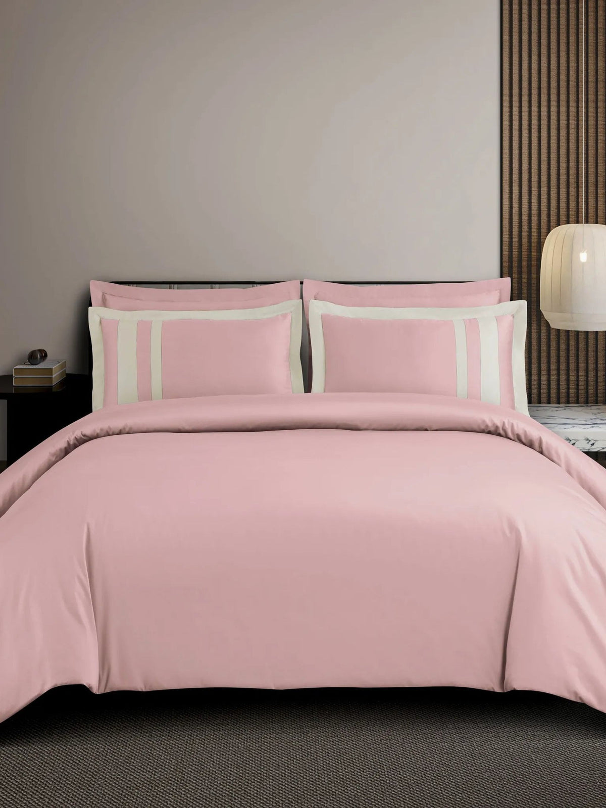 Blush-pink cotton bedsheet set with a cream block-stripe border on the pillow covers, styled on a bed