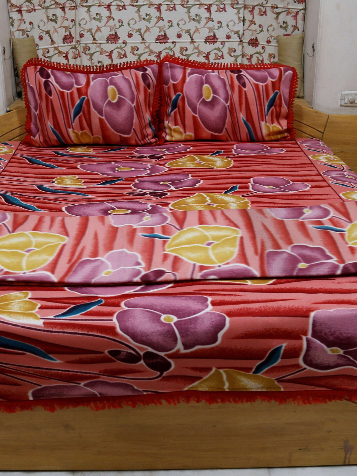 Coral-red blanket set with a mauve-purple and mustard-yellow poppy floral print, spread over a bed with matching pillow covers