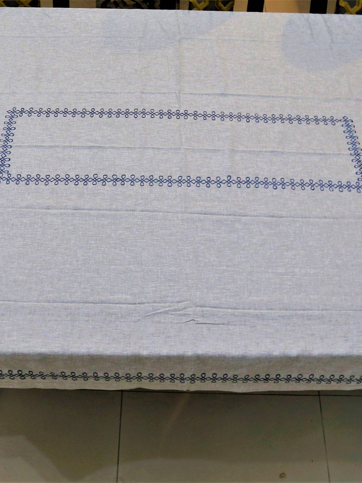 Light grey linen table cover with a navy embroidered scallop-chain border pattern