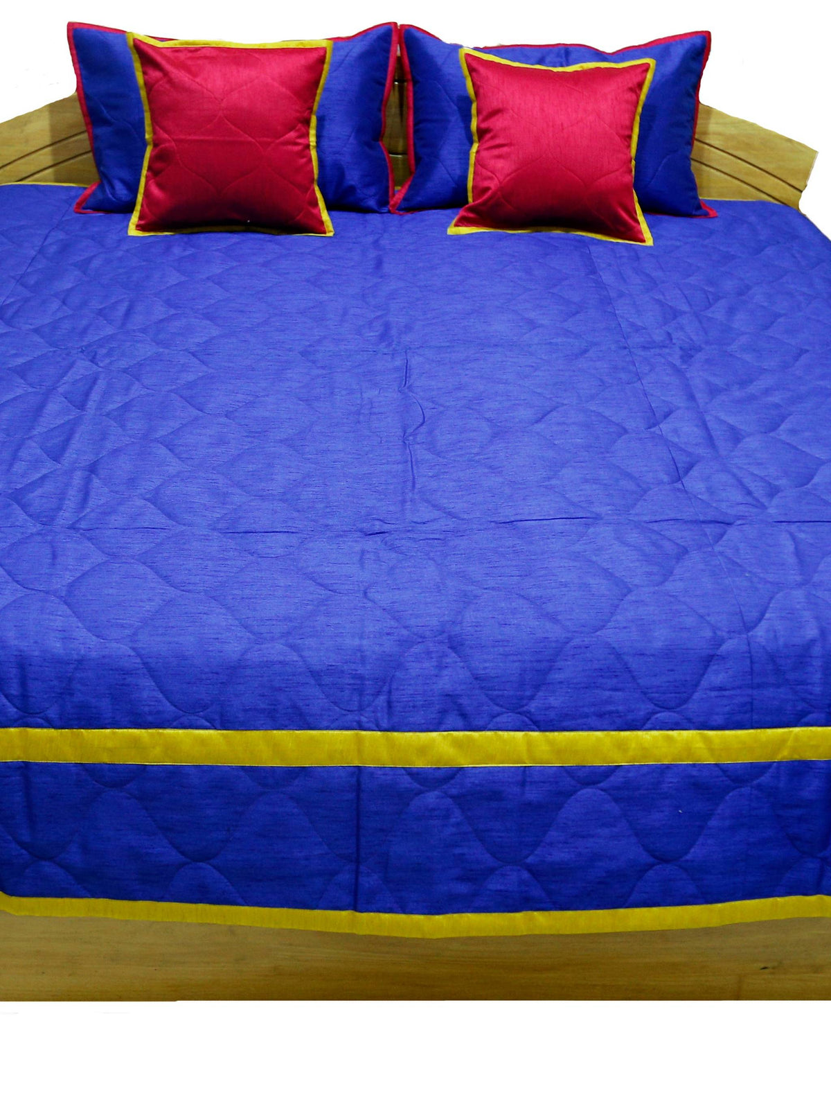 Royal blue quilted bedcover with gold border and crimson cushion covers, straight view