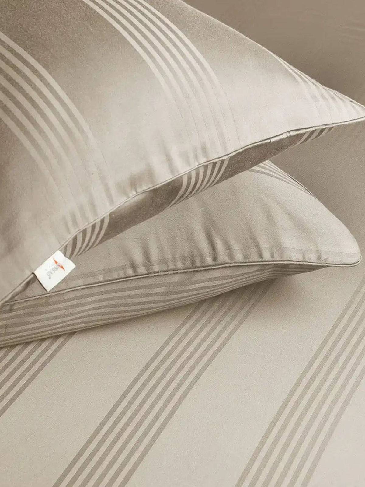 Two pale greige satin stripe pillow covers on the matching bedding, close-up