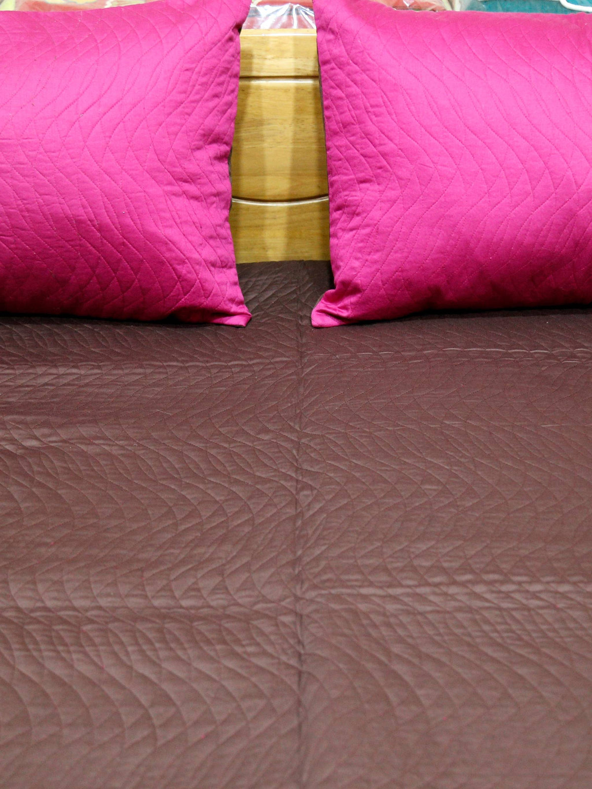 Close-up of magenta pillow covers on the aubergine quilted bedcover