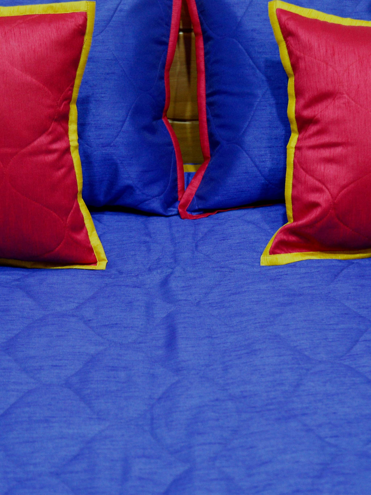 Close-up of crimson gold edged cushion covers on the royal blue quilted bedcover