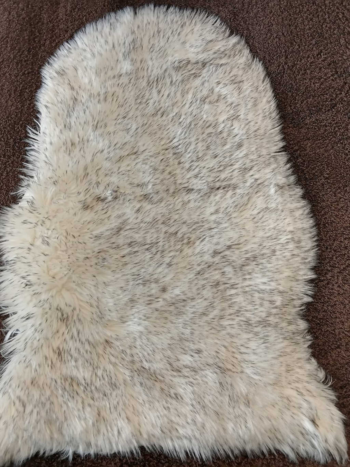 Grey-tipped cream faux sheepskin bedside runner laid on a brown carpet