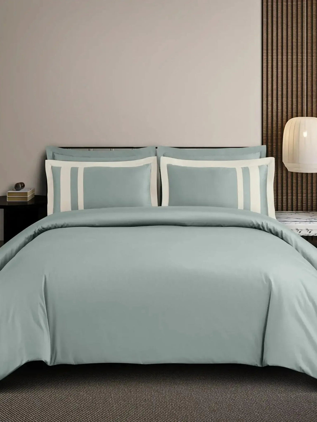Sage-green cotton bedsheet set with a white block-stripe border on the pillow covers, styled on a bed