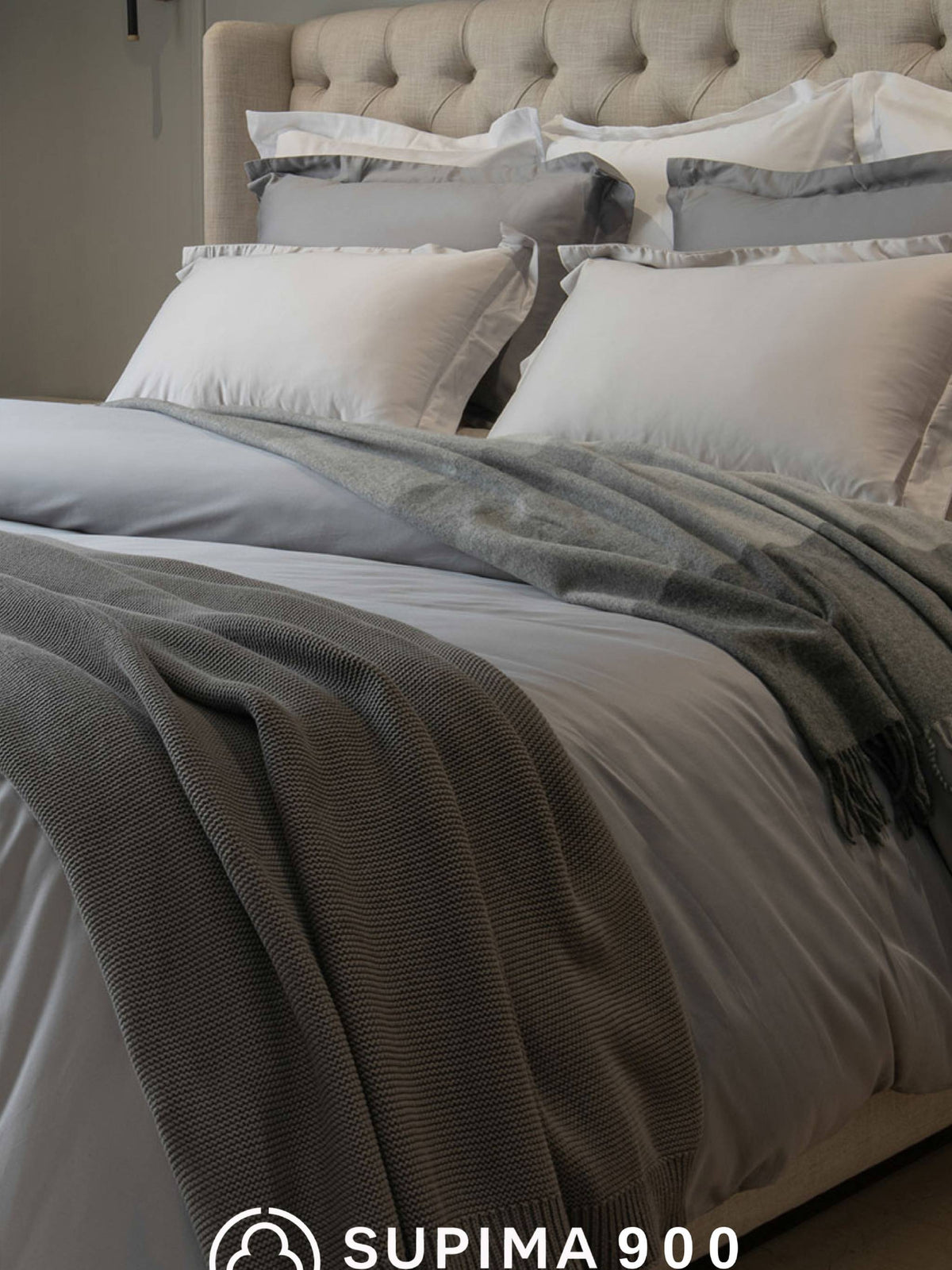 Grey and white Supima 900 bedding made up on a tufted bed