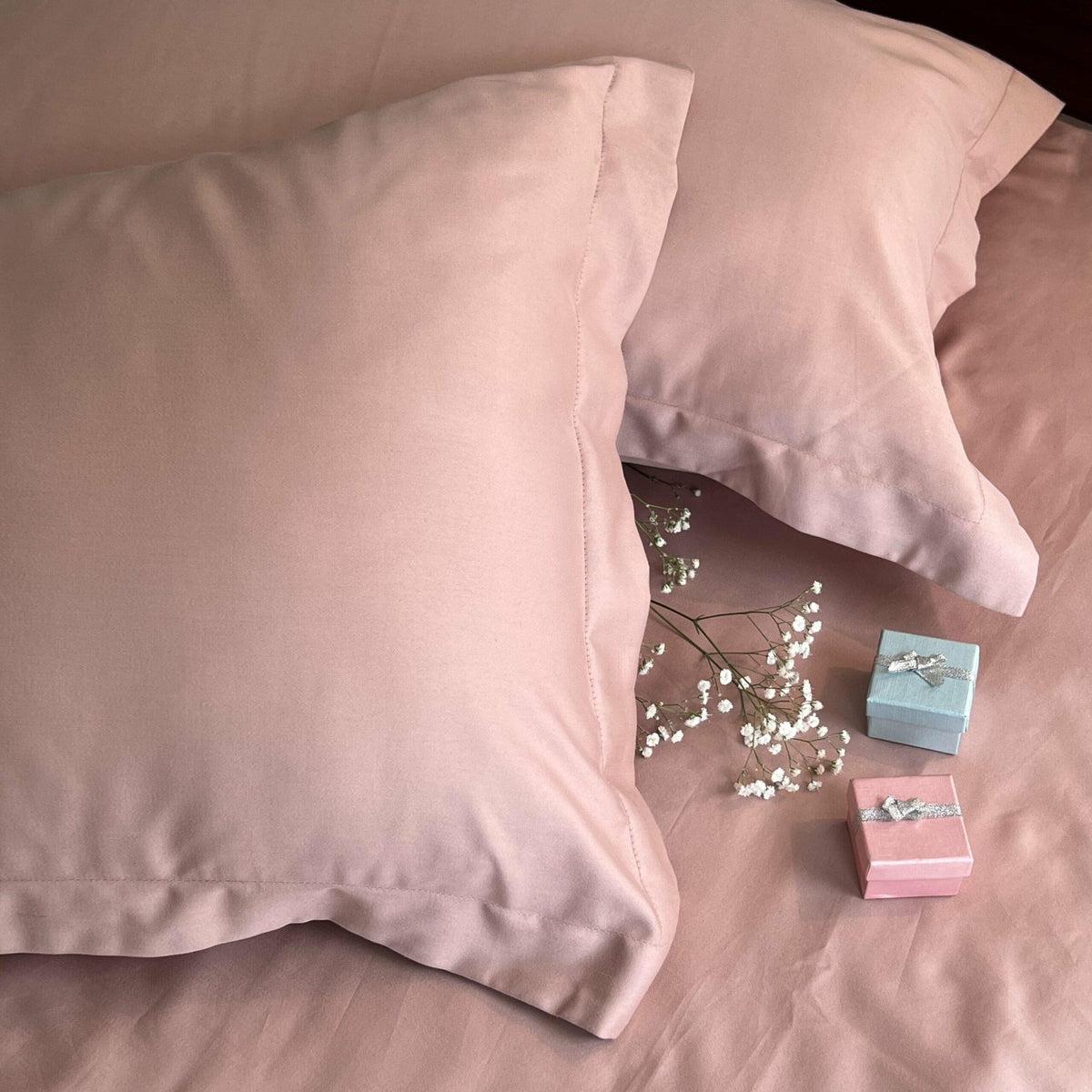 Close-up of dusty rose-pink satin pillow covers on a bed with dried baby's breath flowers and gift boxes