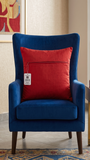 Red embroidered polysilk cushion cover with golden ornamental border design on a blue accent chair