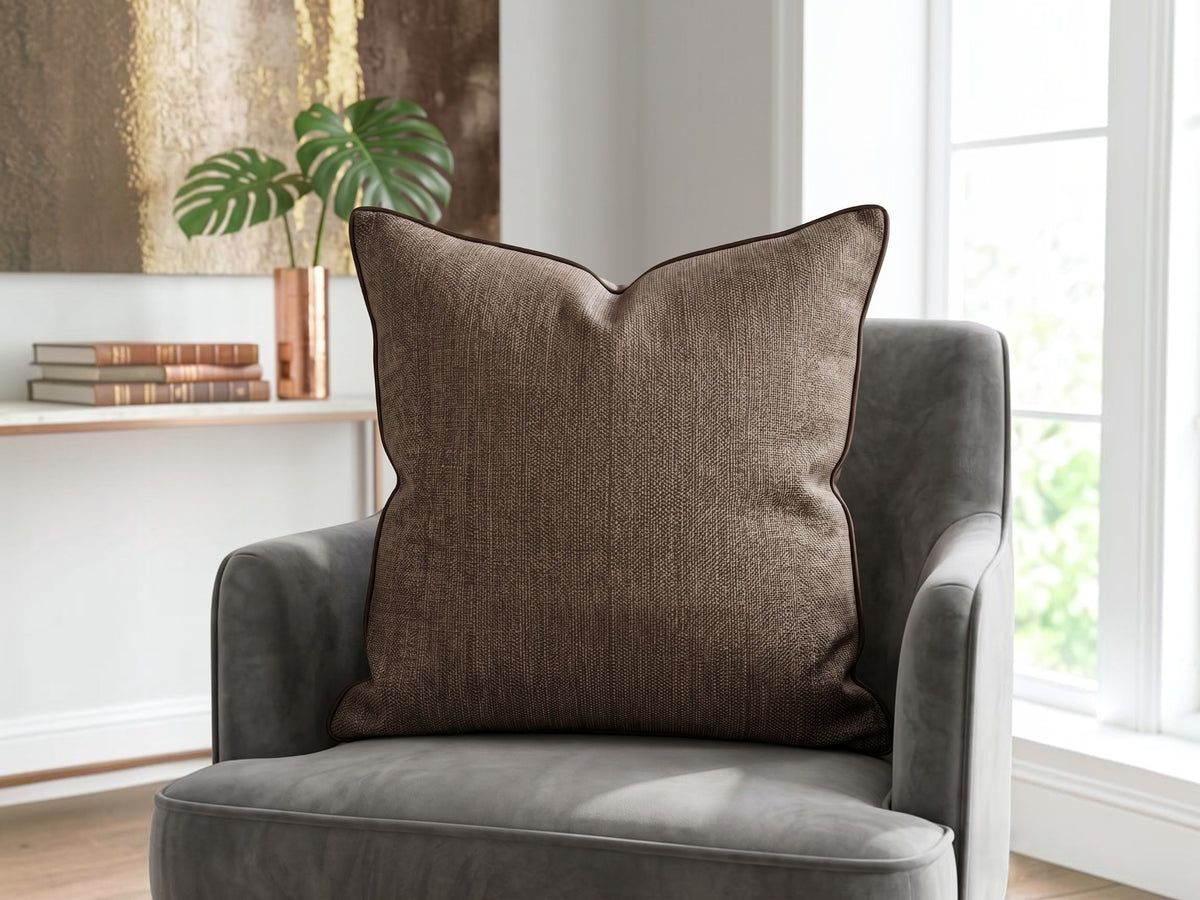 Textured brown woven cushion cover with piped edge on a grey armchair