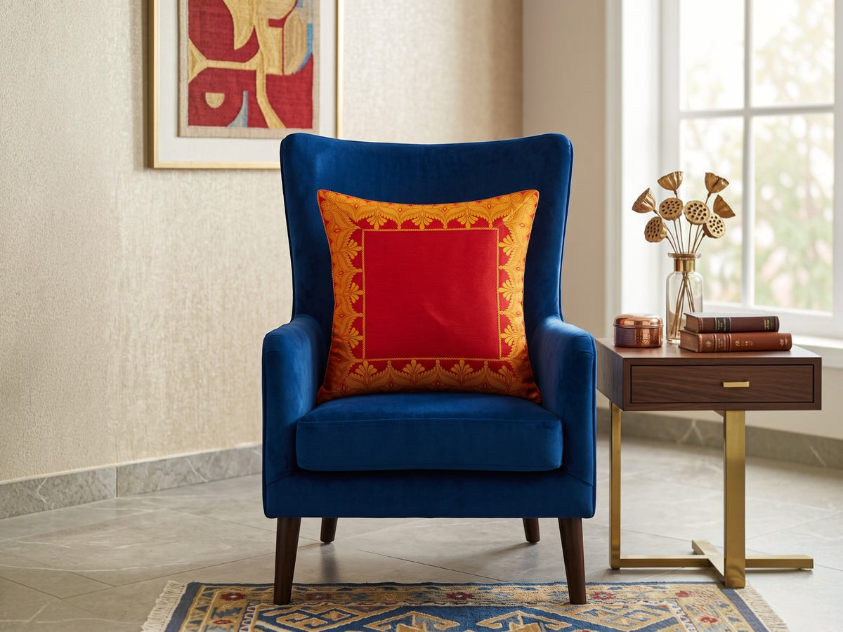 Red embroidered polysilk cushion cover with golden ornamental border design on a blue accent chair