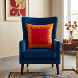 Red embroidered polysilk cushion cover with golden ornamental border design on a blue accent chair