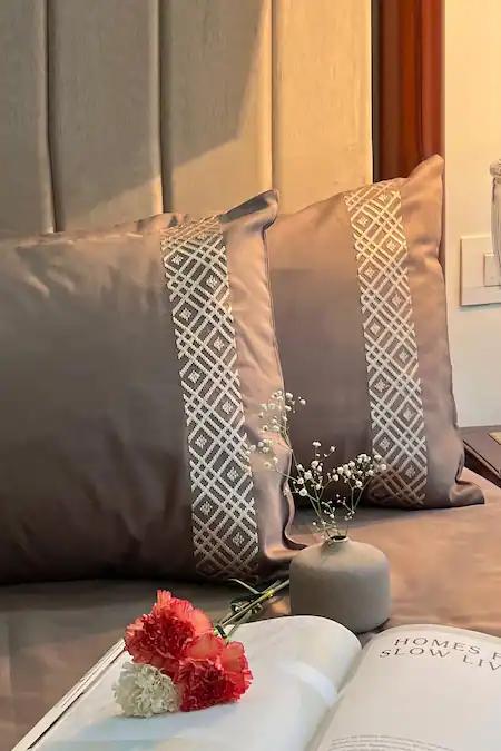 Mauve taupe pillow covers with a white diamond lattice embroidered band on a bed