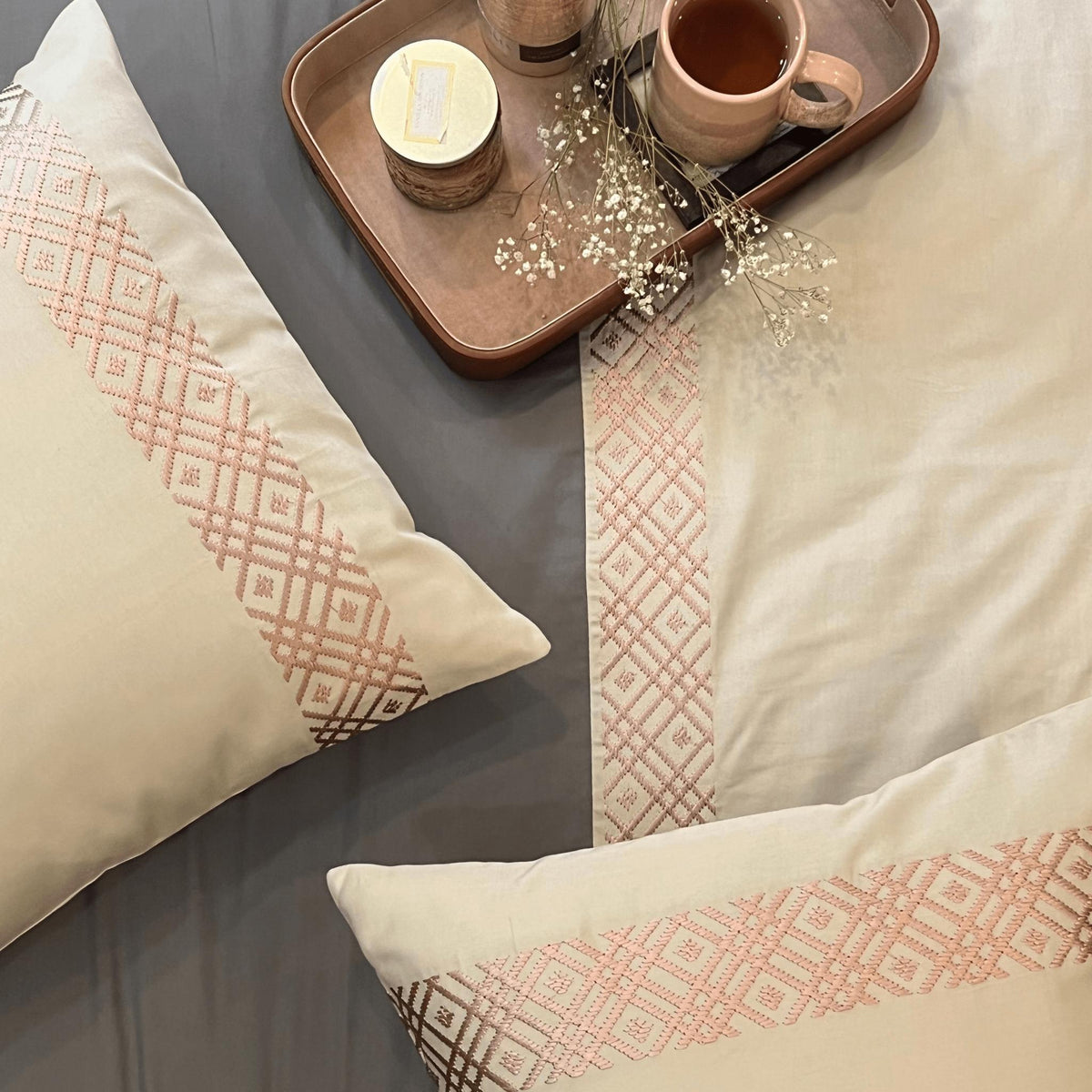 Cream pillows with a rose geometric embroidered band on charcoal sheets, Beige Classic