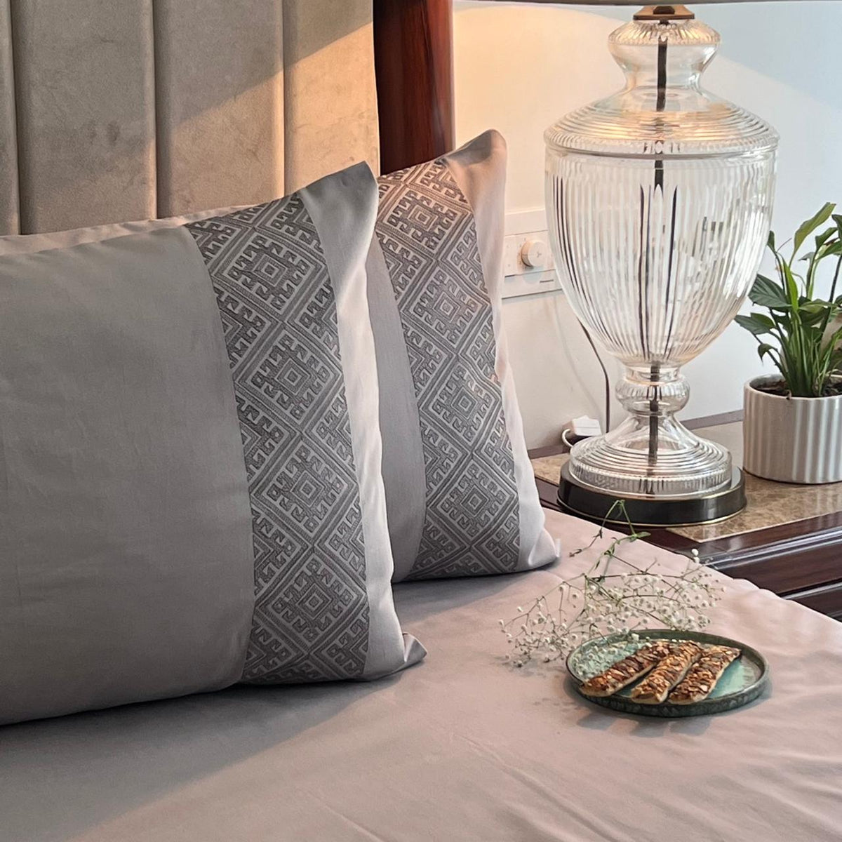 Two silver grey embroidered-panel pillows beside a lamp, Silver Arcane Collection