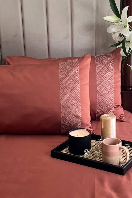 Terracotta bedsheet and pillow covers with a beige diamond-lattice embroidered band, styled on a bed with candles, a mug, and white lilies