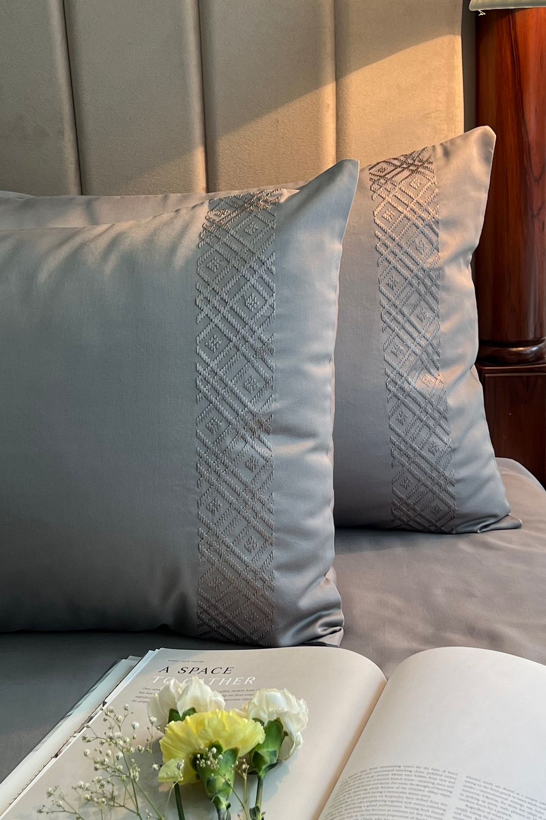 Two silver grey pillow covers with diamond bands against a padded headboard