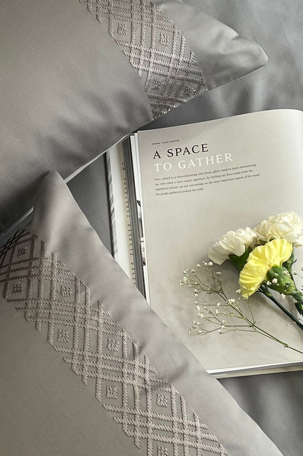 Silver grey pillow covers with a woven diamond band, magazine and yellow carnations
