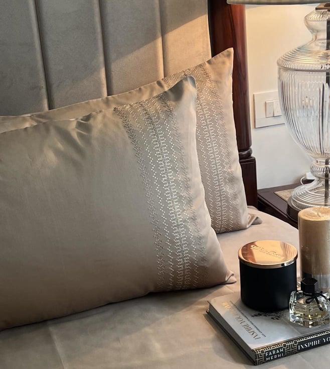Close-up of beige satin pillow covers with a dotted vertical-stripe embroidered band, styled on a bed with a candle and book