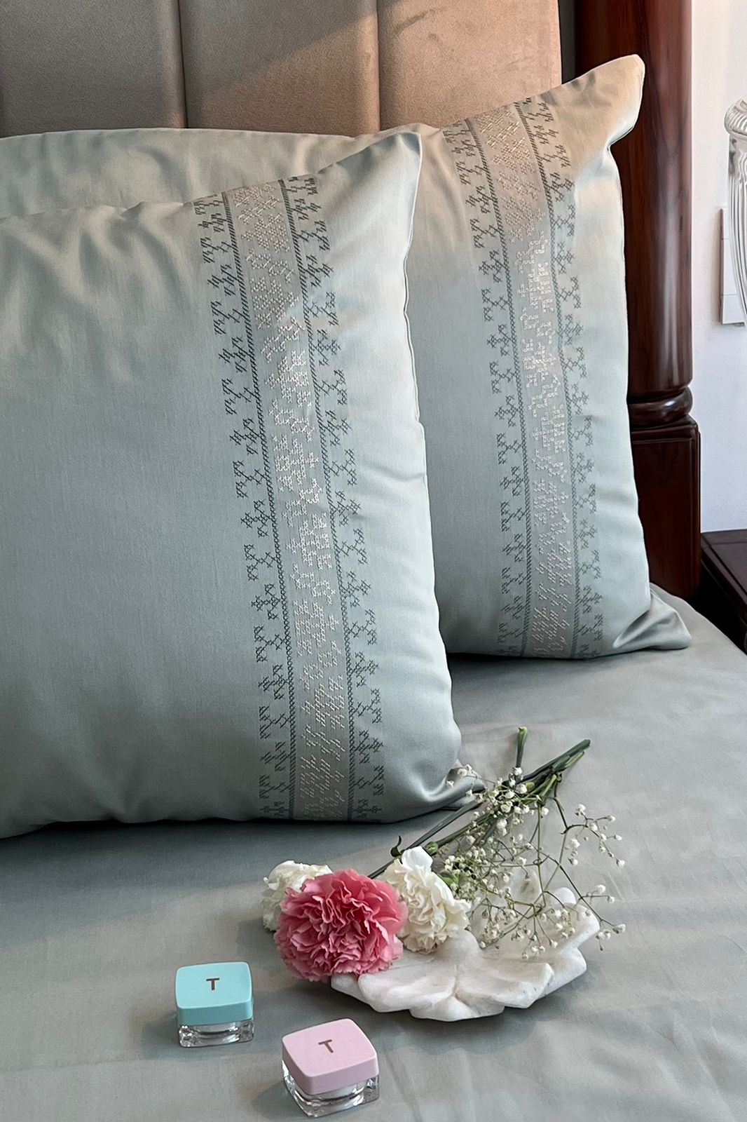 Pale sage pillow covers with grey and silver cross-stitch bands on matching bedding