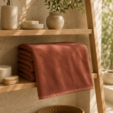 Brown plain cotton bath towel folded on a wooden bathroom shelf
