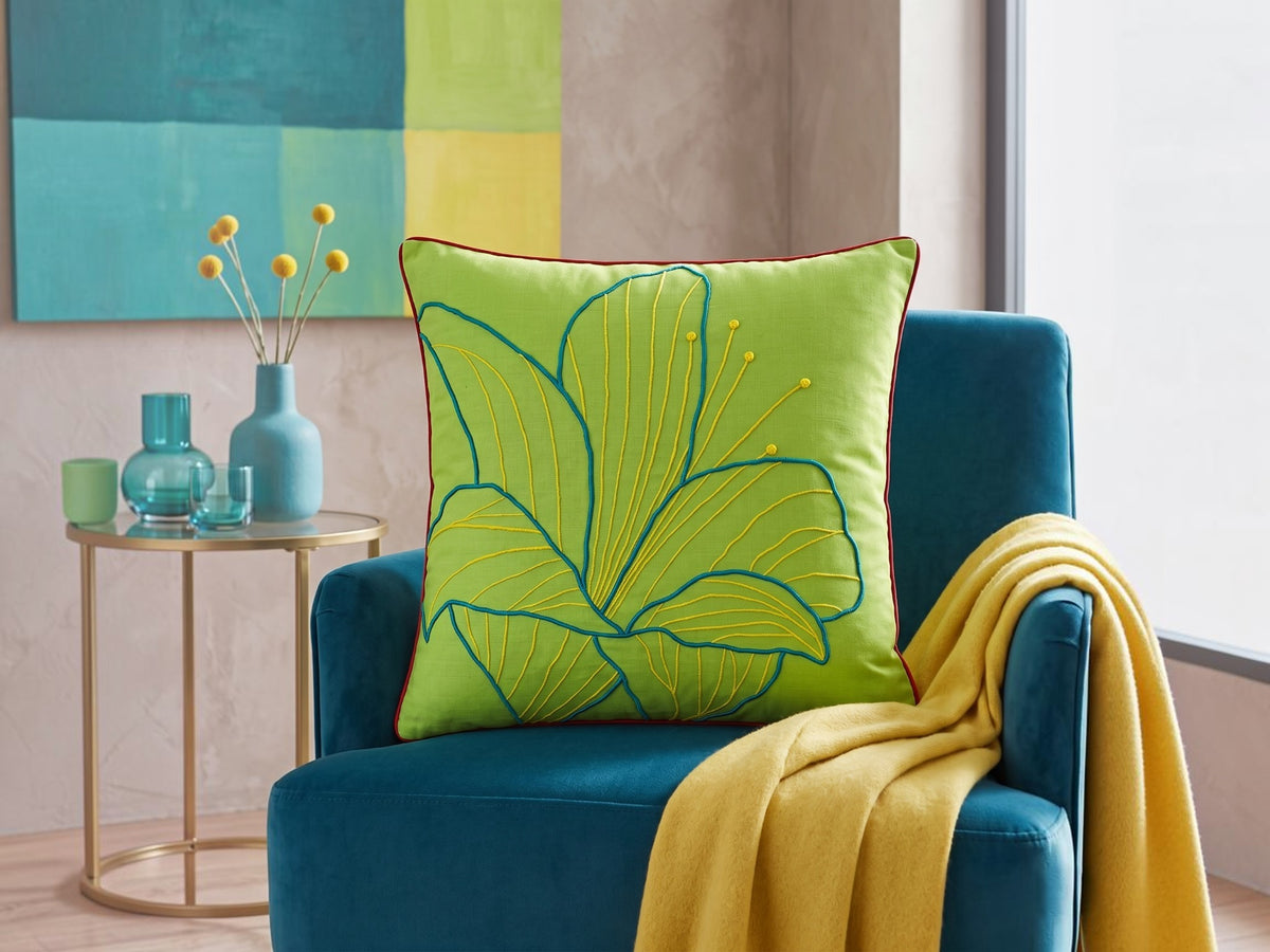 Lime green cushion cover with a teal outline leaf embroidery on a blue armchair
