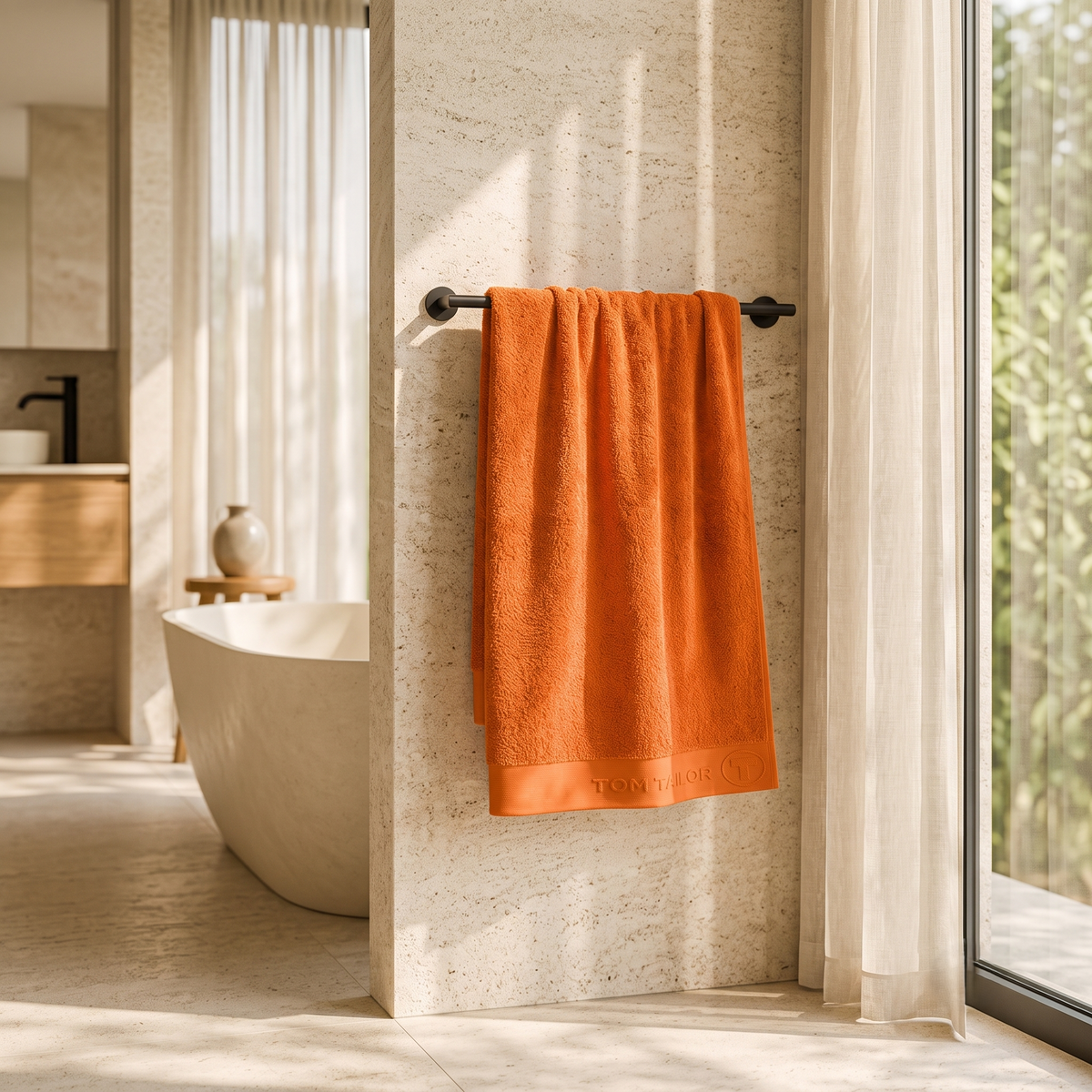 Orange cotton bath towel with woven border hanging on a towel rail in a modern bathroom 