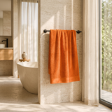 Orange cotton bath towel with woven border hanging on a towel rail in a modern bathroom 