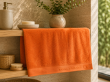 Orange cotton bath towel with woven border placed in a  modern bathroom