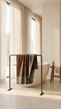 Absorbent brown cotton bath towel with floral border displayed on a modern towel stand